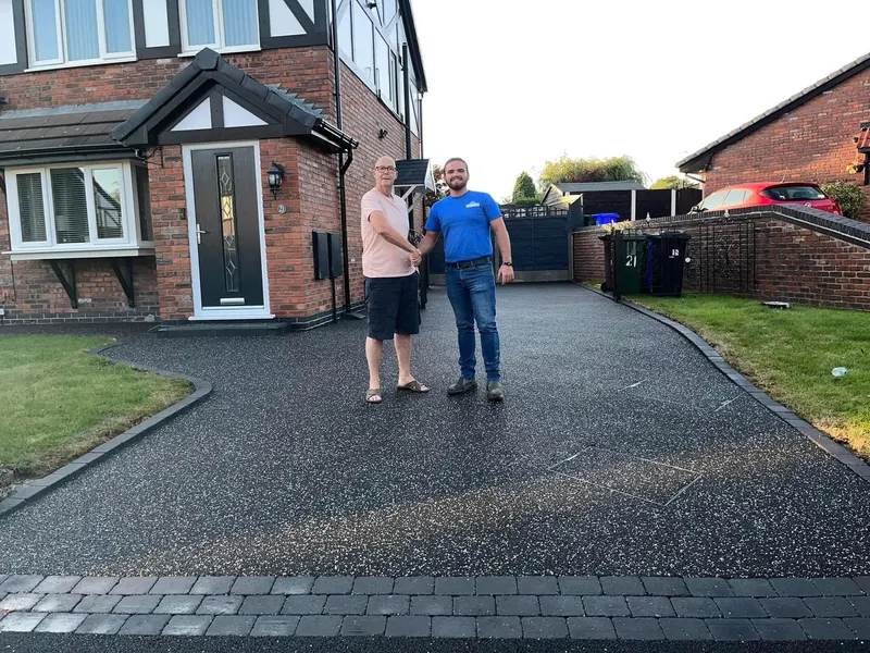 Charcoal resin bound driveway with block paving borders as a customer shakes hands with an installer in front of a red brick house.