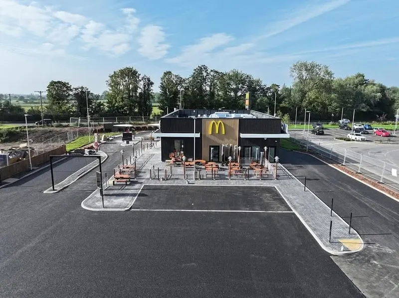 Aerial view of a large fresh black tarmac car park and drive-thru lanes with white bay markings, block-paved walkways, and a fast-food restaurant building.