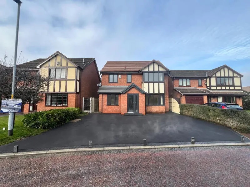 Smooth black tarmac front driveway edged with grey stone setts and inset ground lights, in front of a red brick house with dark grey windows.